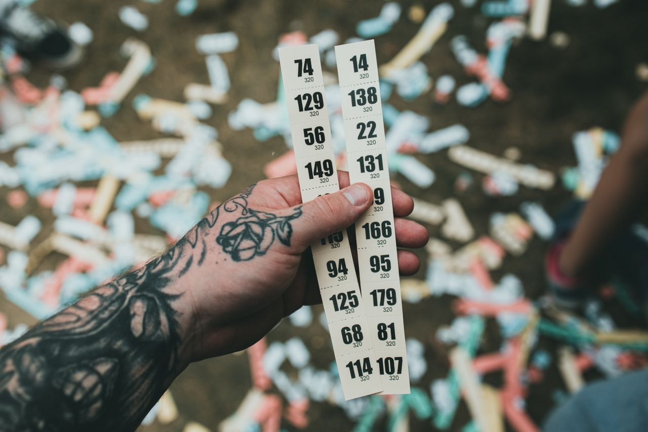 Close-up of a tattooed hand holding raffle tickets amidst confetti at a festival setting.