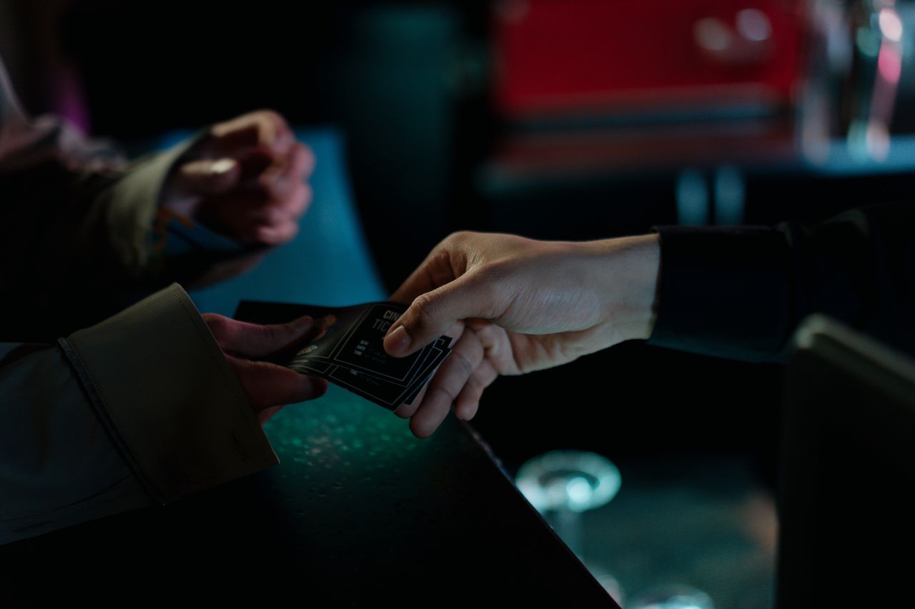 about-02 Hands exchanging movie theater tickets indoors, capturing a cinematic moment.