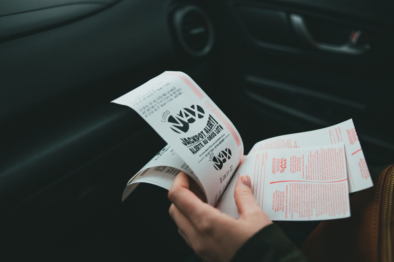 about-01 Close-up of hands holding Lotto Max papers inside a car, symbolizing luck and chance.